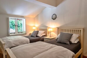 A bedroom with two beds, a window with a fire escape sign, and a wall-mounted light fixture. - Exmoor Retreat Near the Harbor (Lynmouth)