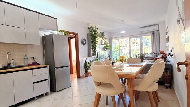 A modern kitchen with white cabinets, a stainless steel refrigerator, and a dining area with a wooden table and chairs. - Spacious SeaView Apartment in the heart of Saranda (Saranda)