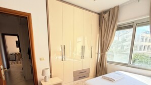 A bedroom with a large bed, a wardrobe, a nightstand, and a view of buildings outside. - Spacious SeaView Apartment in the heart of Saranda (Saranda)