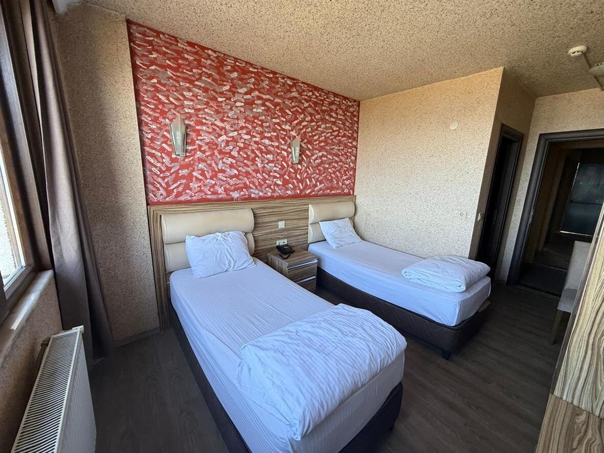 Ein Hotelzimmer mit zwei Einzelbetten, einer roten Wand mit Muster und einem Fenster mit Vorhängen.
