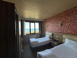 Een hotelkamer met twee bedden, een groot raam met uitzicht op het strand en een rode, gemêleerde wand.