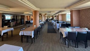 A spacious restaurant with multiple tables and chairs, a central aisle, and a patterned wall on one side. - otel ustabaş (Hopa)
