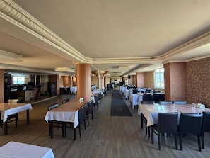 A spacious restaurant with multiple tables and chairs, a central aisle, and a patterned wall on one side. - otel ustabaş (Hopa)