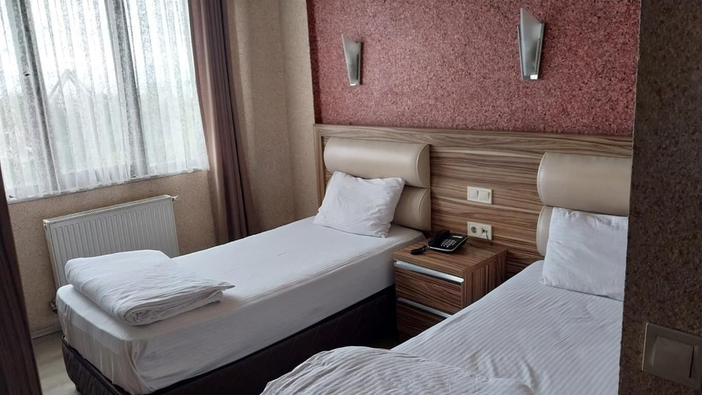 Ein Hotelzimmer mit zwei Einzelbetten, einem Nachttisch mit Telefon und einem Fenster mit Vorhängen.