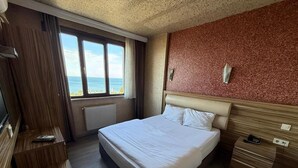 A hotel room with a bed, a desk, a window with a view, and a wooden wall. - otel ustabaş (Hopa)