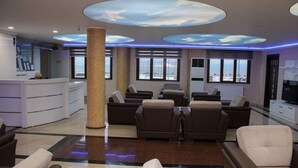 A hotel lobby with a reception desk, seating area, and large windows offering a city view. - otel ustabaş (Hopa)