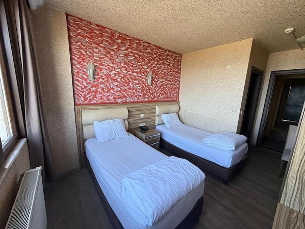 A hotel room with two beds, a large window, a radiator, and a decorative wall.