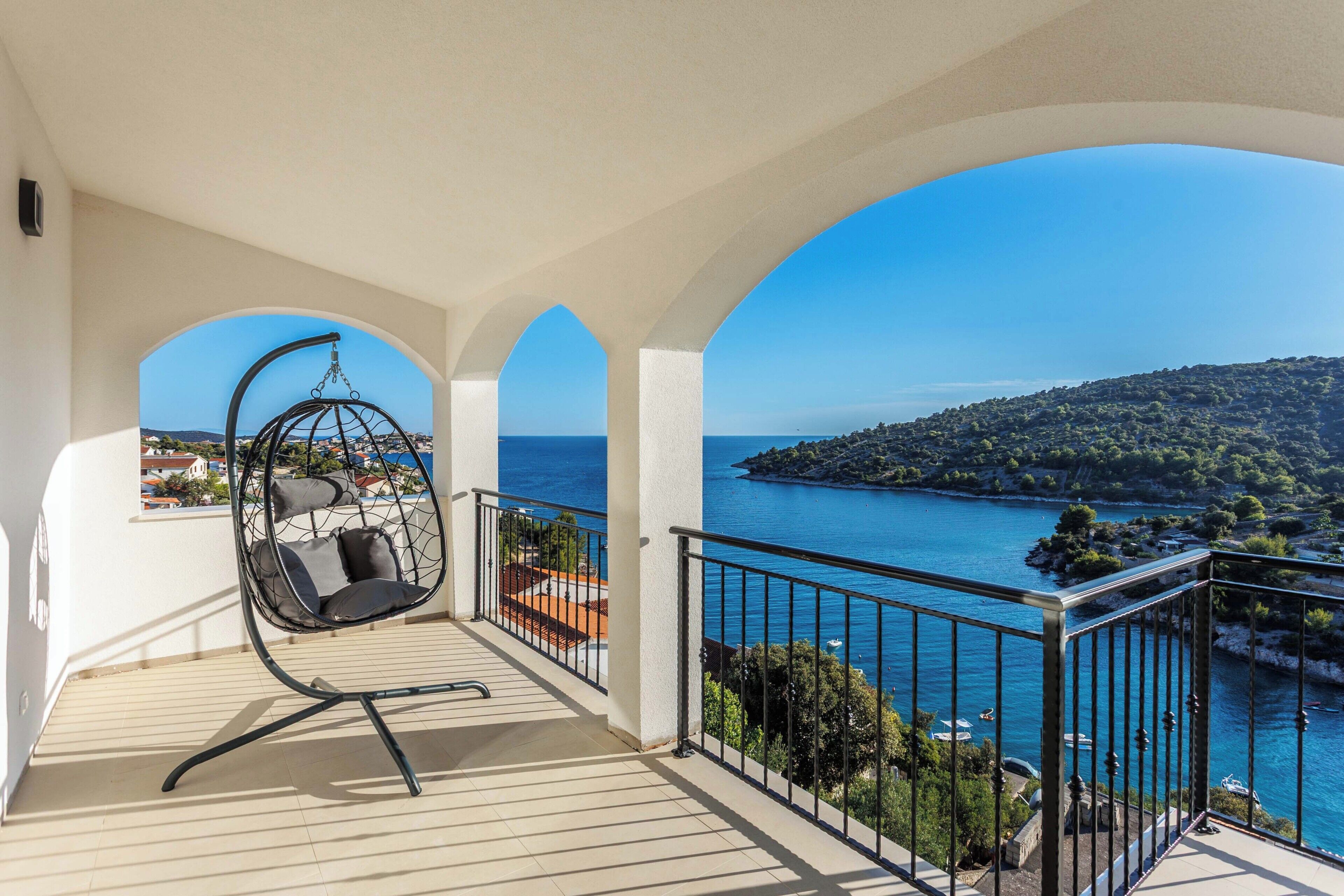 A balcony with a hanging chair, a view of the sea, and a mountainous landscape.