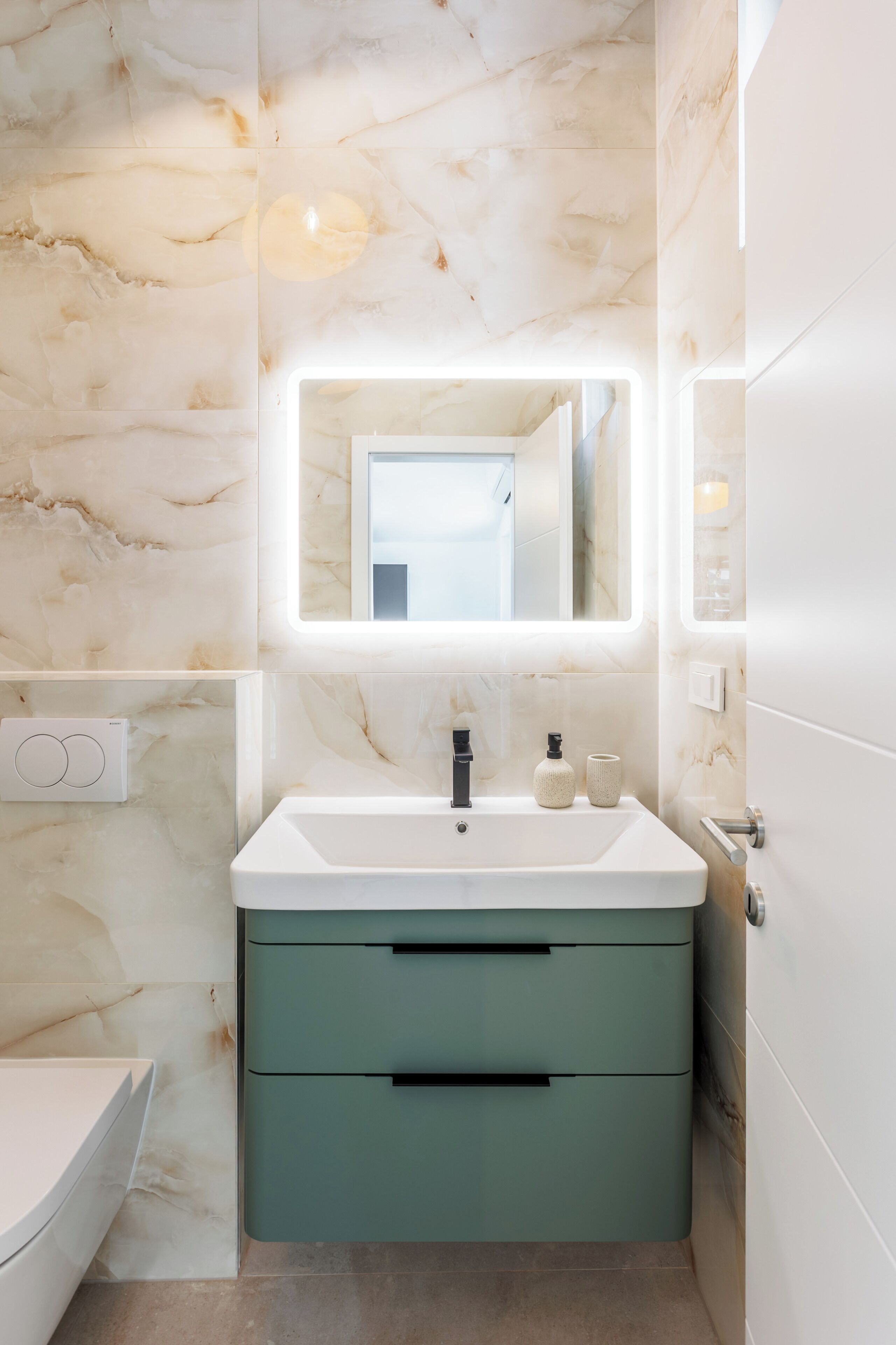 A bathroom with a marble wall, a white sink with a faucet, a mirror, and a green cabinet.