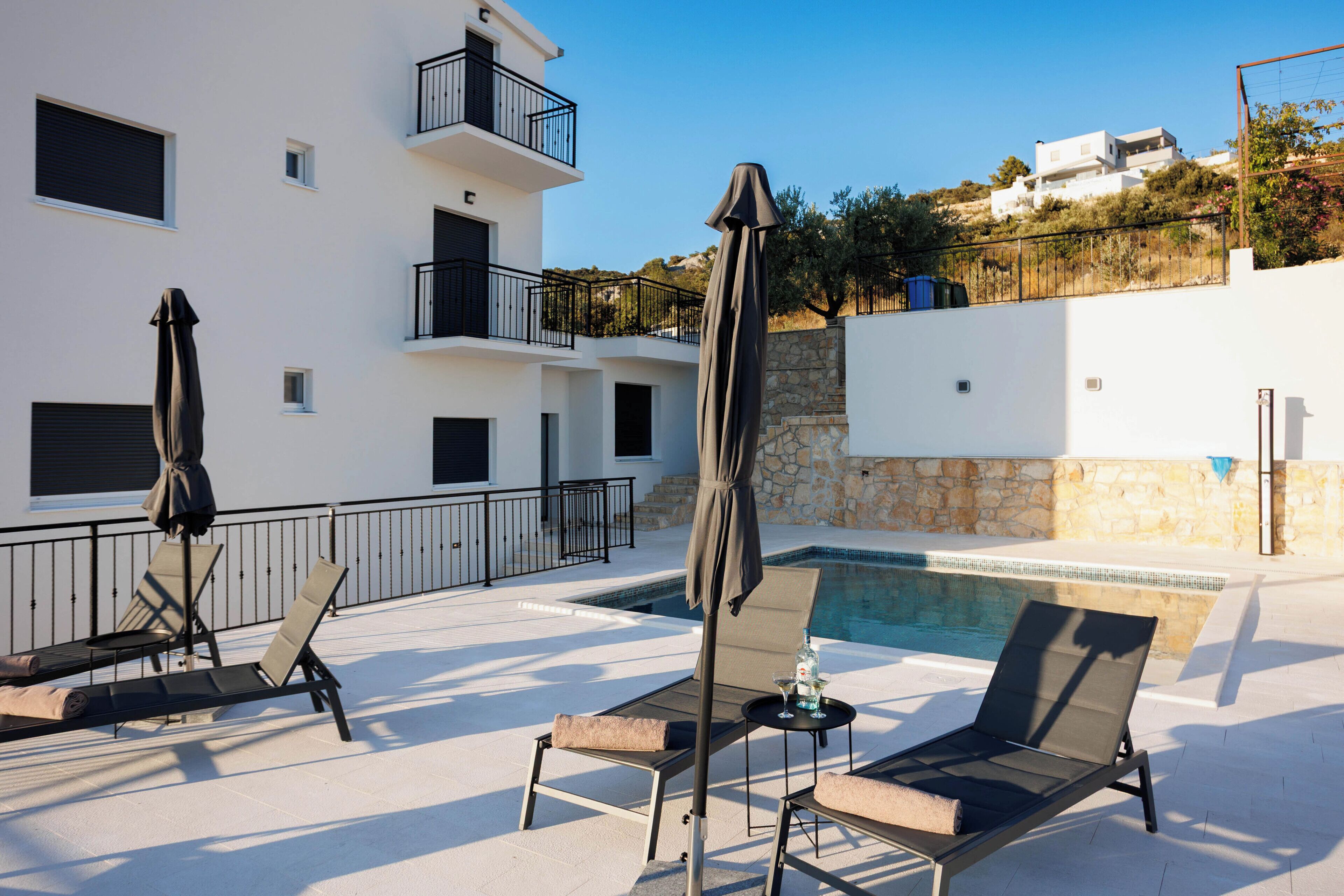 Un espace piscine aménagé sur le toit, avec des chaises longues et des parasols, un mur en pierre et un bâtiment en arrière-plan.