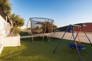A backyard with a trampoline, a swing set, and artificial grass.