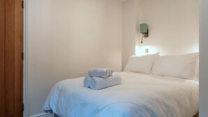 Um quarto com uma cama, uma luminária na parede e uma porta de madeira.
