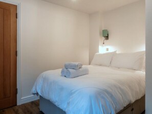 A bedroom with a bed, a wall-mounted light, and a wooden door. - Contemporary Cornwall Retreat for Groups (Ross-on-Wye)