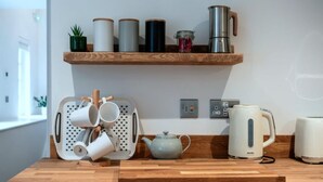 Uma cozinha com bancada de madeira, cafeteira, chaleira e suporte para canecas.