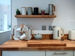 A kitchen with a wooden countertop, a coffee maker, a kettle, and a mug holder. - Contemporary Cornwall Retreat for Groups (Ross-on-Wye)