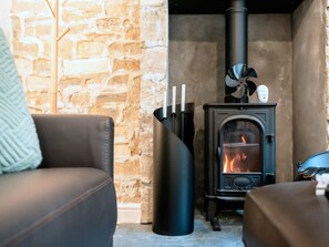 A cozy living room with a stone wall, a black fireplace with a visible fire, and a modern black heater. - Contemporary Cornwall Retreat for Groups (Ross-on-Wye)