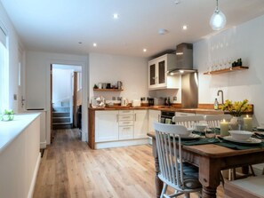 A modern kitchen with wooden flooring, white cabinetry, and a dining area with a wooden table and chairs. - Contemporary Cornwall Retreat for Groups (Ross-on-Wye)
