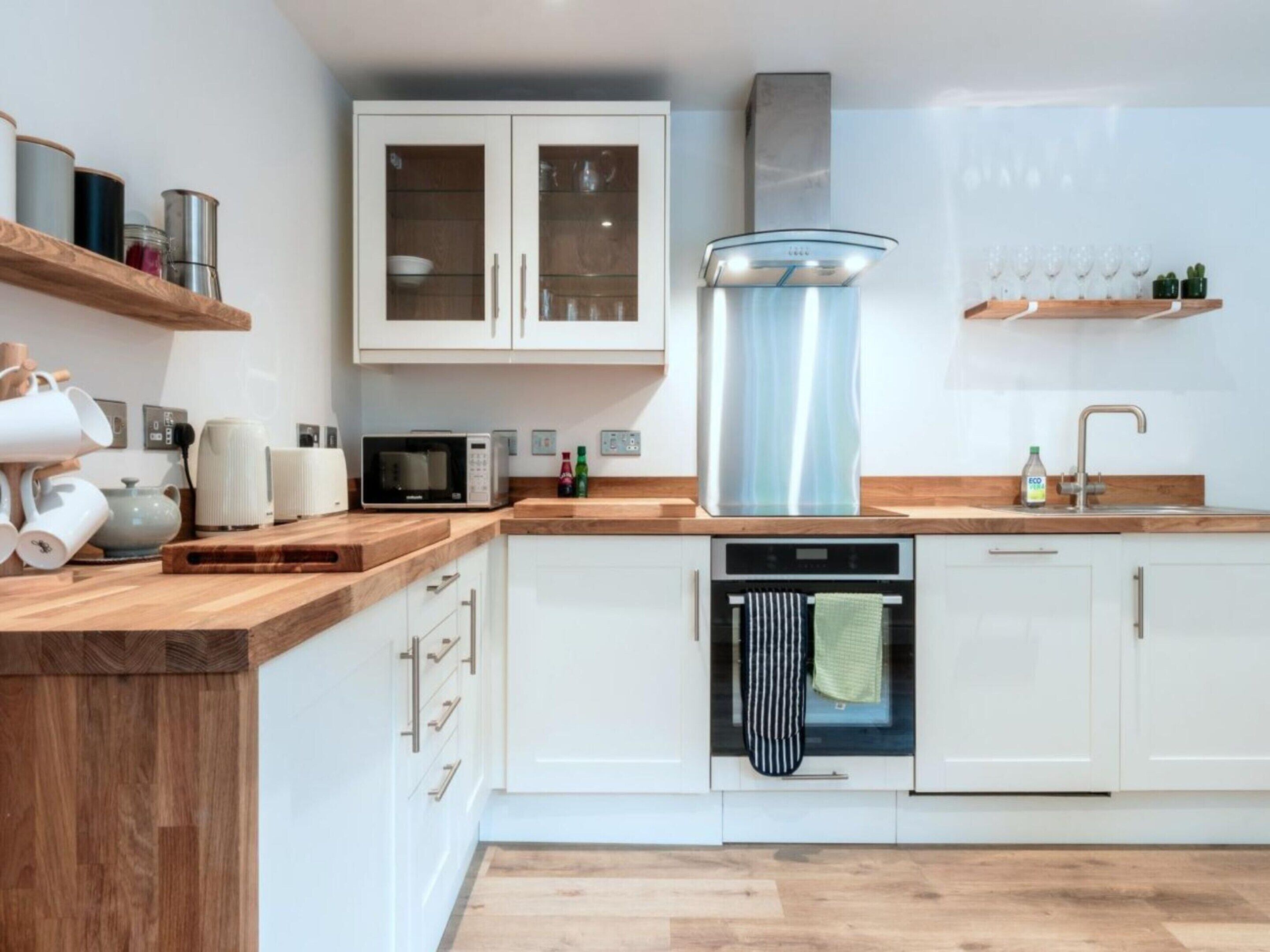Una cocina moderna con armarios blancos, extractor de acero inoxidable, microondas y lavavajillas.