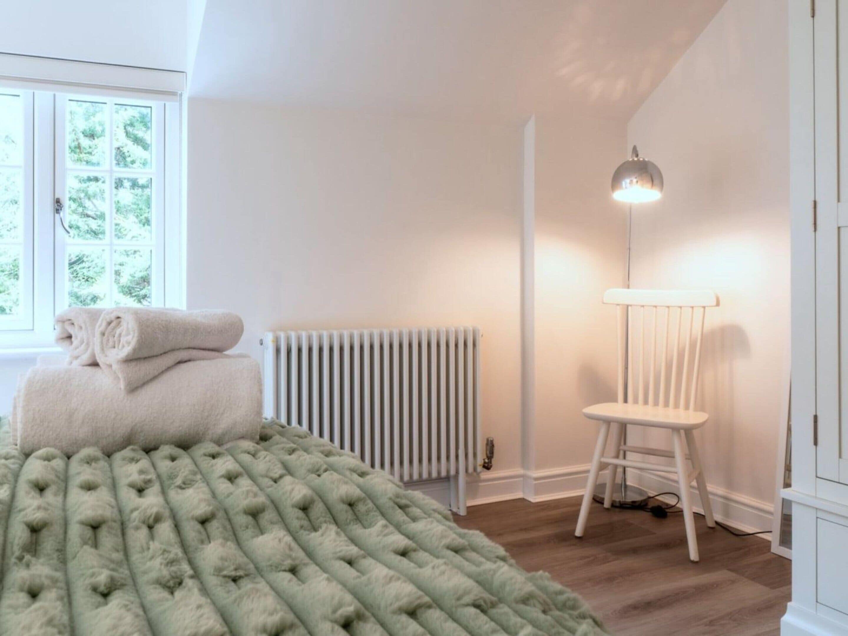 Une pièce comprenant un lit, un radiateur, une chaise et un lampadaire.