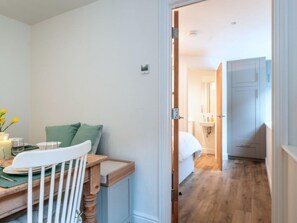 Ein Zimmer mit Esstisch, Stühlen, einem Bett, einem Kleiderschrank und einem durch eine offene Tür einsehbaren Badezimmer.