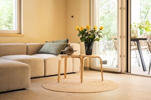 A living room with a sofa, a small table, a vase with flowers, and a view through a glass door. - Villetta Malner – Luxury Villa with Private Pool (Garica)