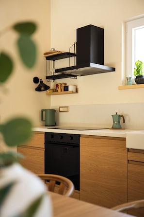 A modern kitchen with a black range hood, wooden cabinets, and a window with a plant. - Villetta Malner – Luxury Villa with Private Pool (Garica)