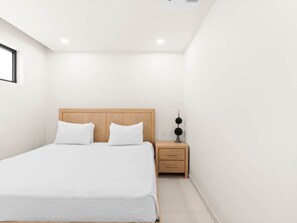 A minimalist bedroom with a bed, bedside table, and a wall-mounted light fixture. - D436 - Lovely apartment with balcony & lagoon view (Cole Bay)