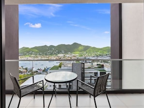Een balkon met uitzicht op een kustplaats, een tafel en twee stoelen.