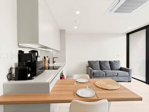 A modern kitchen with a coffee machine, a dining table with plates and cutlery, and a grey sofa in a bright room with a large window. - D436 - Lovely apartment with balcony & lagoon view (Cole Bay)
