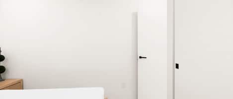 A minimalist hotel room with a bed, a bedside table, a wall-mounted air conditioner, and a door.