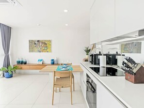 A modern kitchen with white cabinetry, a dining area with a wooden table and chairs, and a kitchen island with a sink and appliances. - A135 - Beautiful one bedroom apartment (Cole Bay)