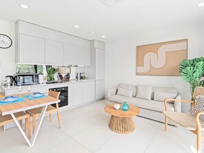 A modern kitchen with white cabinets, a dining area with a wooden table and chairs, a round coffee table, and a living area with a sofa and a large abstract painting. - A135 - Beautiful one bedroom apartment (Cole Bay)