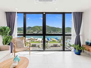 A hotel room with large windows, a wicker chair, a wooden coffee table, and potted plants. - A135 - Beautiful one bedroom apartment (Cole Bay)