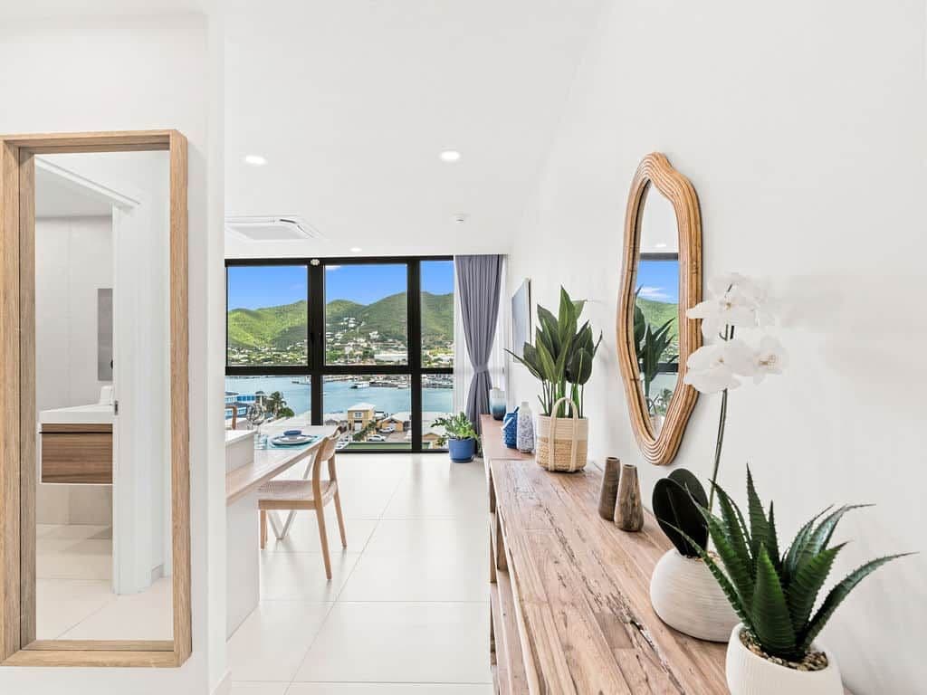 A modern interior with a dining area, a large mirror, and a view of a coastal landscape.