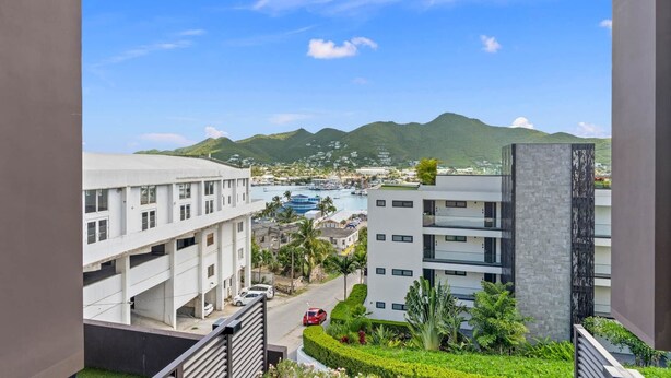 Vista de uma cidade costeira com edifícios modernos, uma marina e montanhas ao fundo.