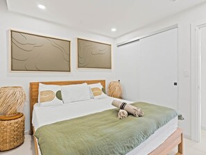 Quarto bem arrumado com uma cama, almofadas, um cobertor verde e duas obras de arte abstratas penduradas na parede.