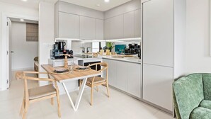 Uma cozinha moderna com armários brancos, uma mesa de jantar com cadeiras e uma poltrona verde.