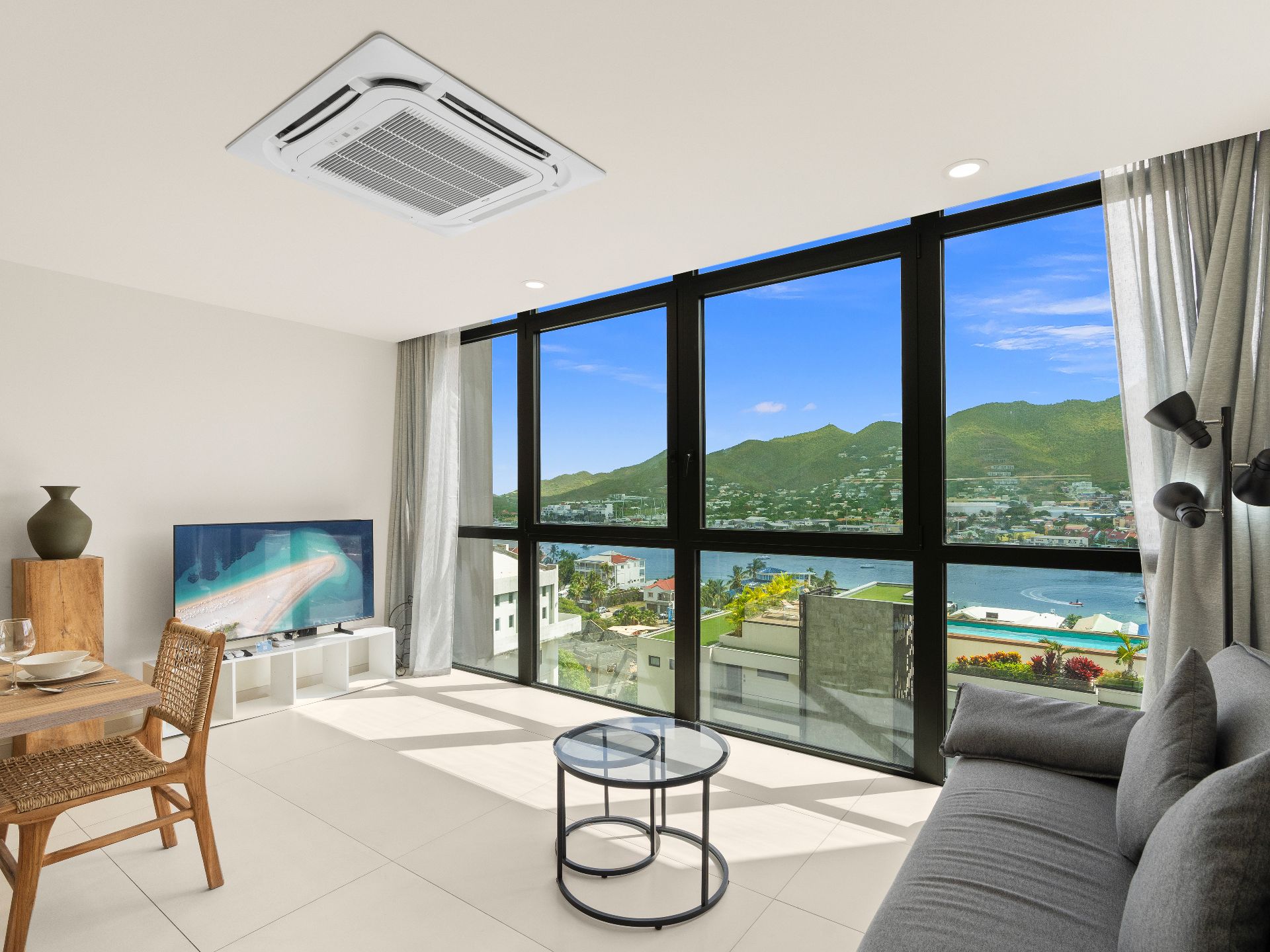 A modern living room with a large window, a flat-screen TV, a dining area with a table and chairs, and a sofa.