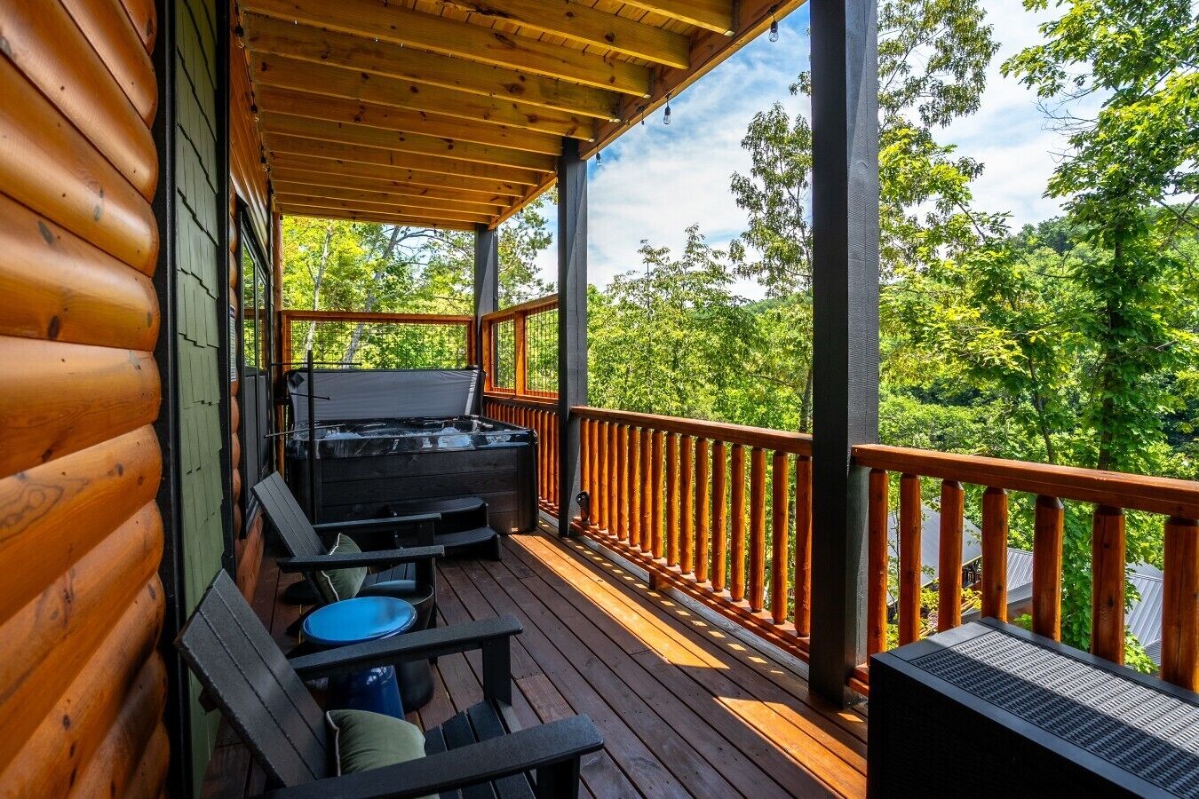 A wooden deck with a hot tub, seating, and a view of a forested area.