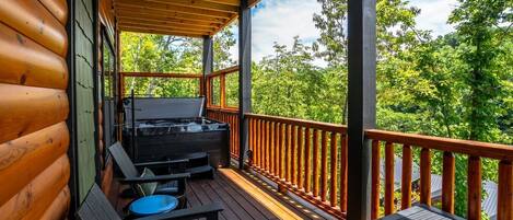 A wooden deck with a hot tub, seating, and a view of a forested area.