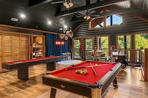 A pool table with balls, a drum set, and a vintage car in a room with wooden floors and a balcony overlooking greenery. - Chrome&Timber|Pool|Sauna|HotTub|FirePit|Sleeps 33 (Sevierville)