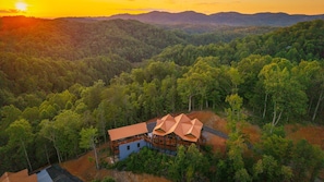 A cabin with a unique geometric roof structure surrounded by dense forest, with a view of distant hills. - Chrome&Timber|Pool|Sauna|HotTub|FirePit|Sleeps 33 (Sevierville)
