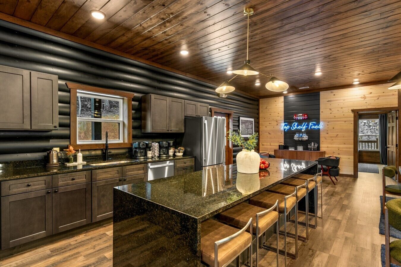 A modern kitchen with a large island, bar stools, and a neon sign.