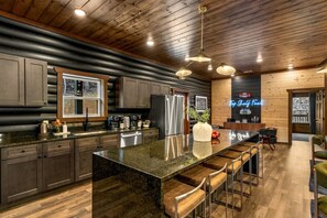 A modern kitchen with a large island, bar stools, and a neon sign. - Chrome&Timber|Pool|Sauna|HotTub|FirePit|Sleeps 33 (Sevierville)