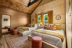Ein gemütliches Schlafzimmer im Blockhausstil mit zwei Betten, einem großen Spiegel und einer Holzbalkendecke.