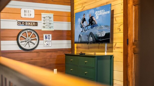 A room with a wooden wall, a television displaying 'Fast & Furious 6', a 'NO SPEED LIMIT' sign, and a 'BEEP BEEP' sign. - Chrome&Timber|Pool|Sauna|HotTub|FirePit|Sleeps 33 (Sevierville)