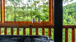 A hot tub with two metal cups on a wooden deck, surrounded by a metal railing and a view of greenery. - Chrome&Timber|Pool|Sauna|HotTub|FirePit|Sleeps 33 (Sevierville)