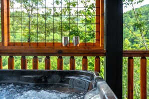 Ein Whirlpool mit zwei Metallbechern auf einer Holzterrasse, umgeben von einem Metallgeländer und Blick ins Grüne.