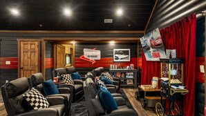 A home theater room with multiple seating areas, a popcorn machine, and a red curtain backdrop. - Chrome&Timber|Pool|Sauna|HotTub|FirePit|Sleeps 33 (Sevierville)