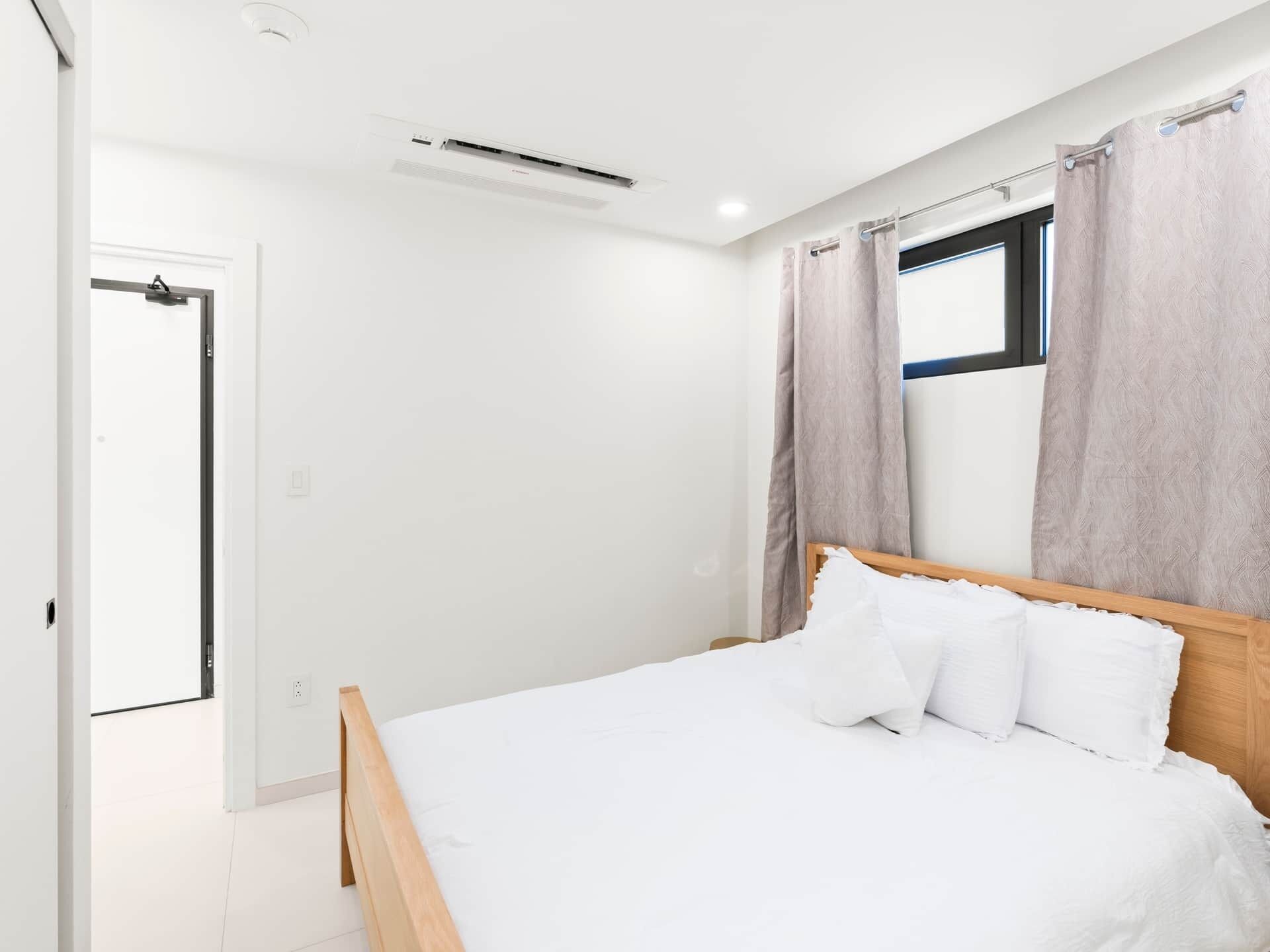 Een slaapkamer met een houten bed, wit beddengoed, een raam met gordijnen en een deur.